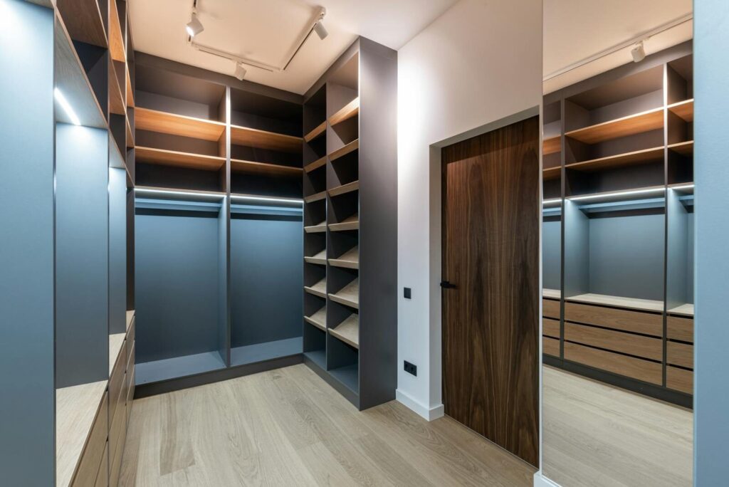 Interior of spacious light wardrobe room with empty shelves near mirror and door