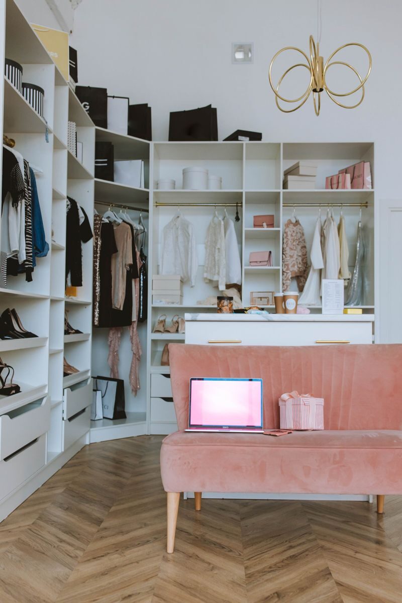 Chic dressing room with open closet, laptop on a pink couch, and stylish decor.